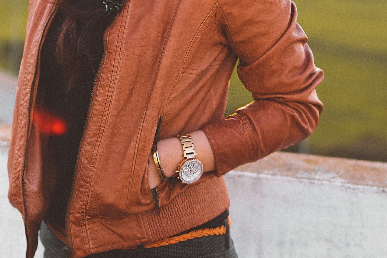 close up image of a woman with her hand in her jacket pocket wearing a diamond studded watch
