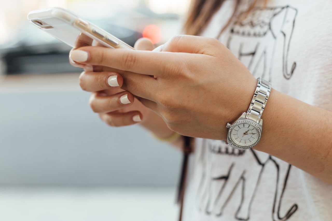 close up image of a woman looking at her phone and wearing a silver, diamond accented watch