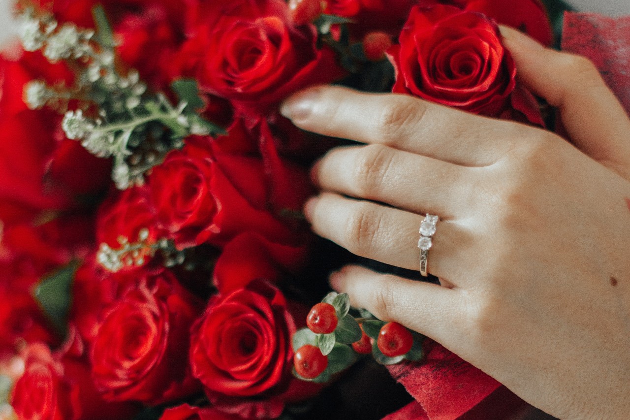 A woman’s hand touches a bouquet of red roses while wearing an anniversary band.