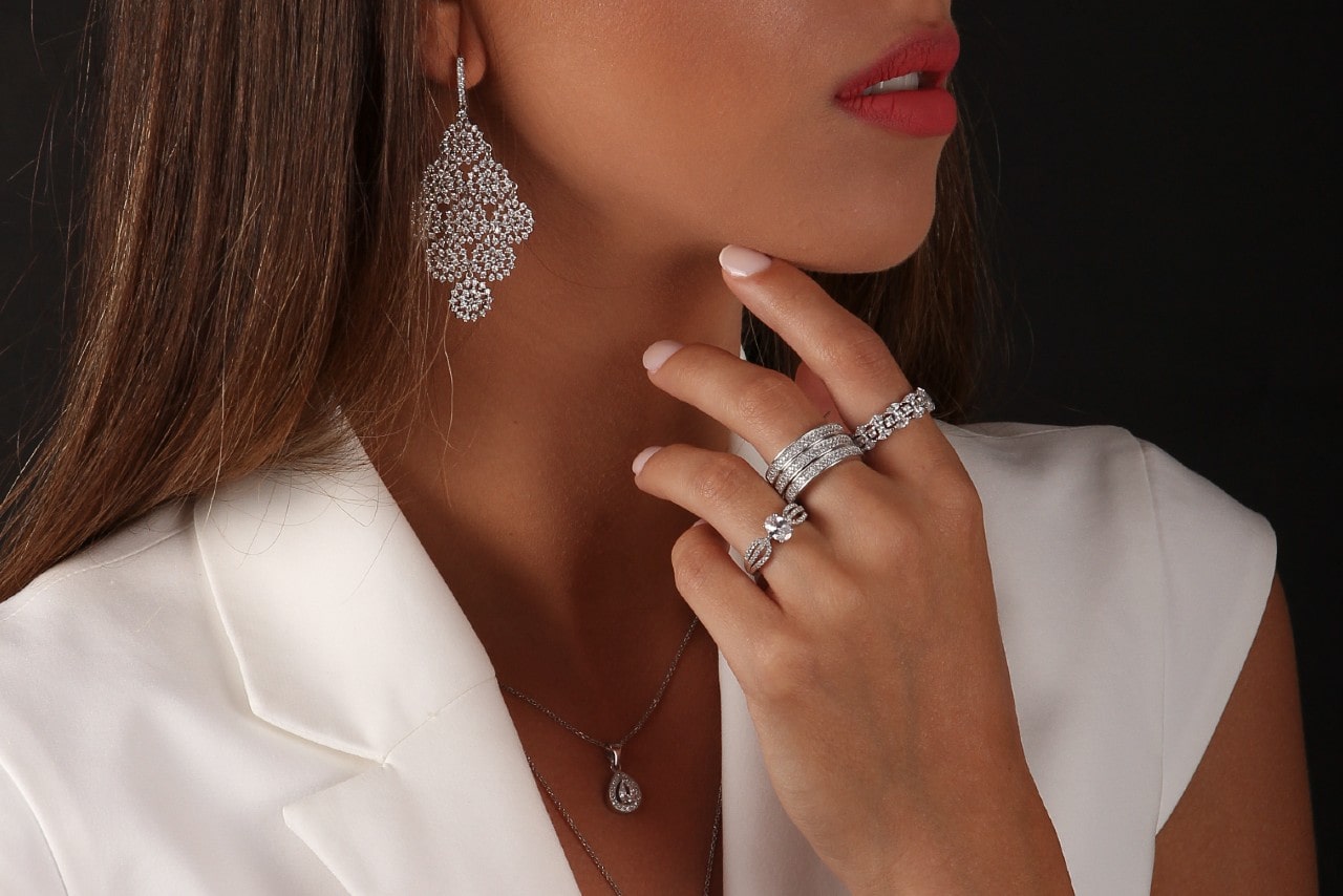 A woman in a white suit jacket showcases multiple diamond jewelry pieces.