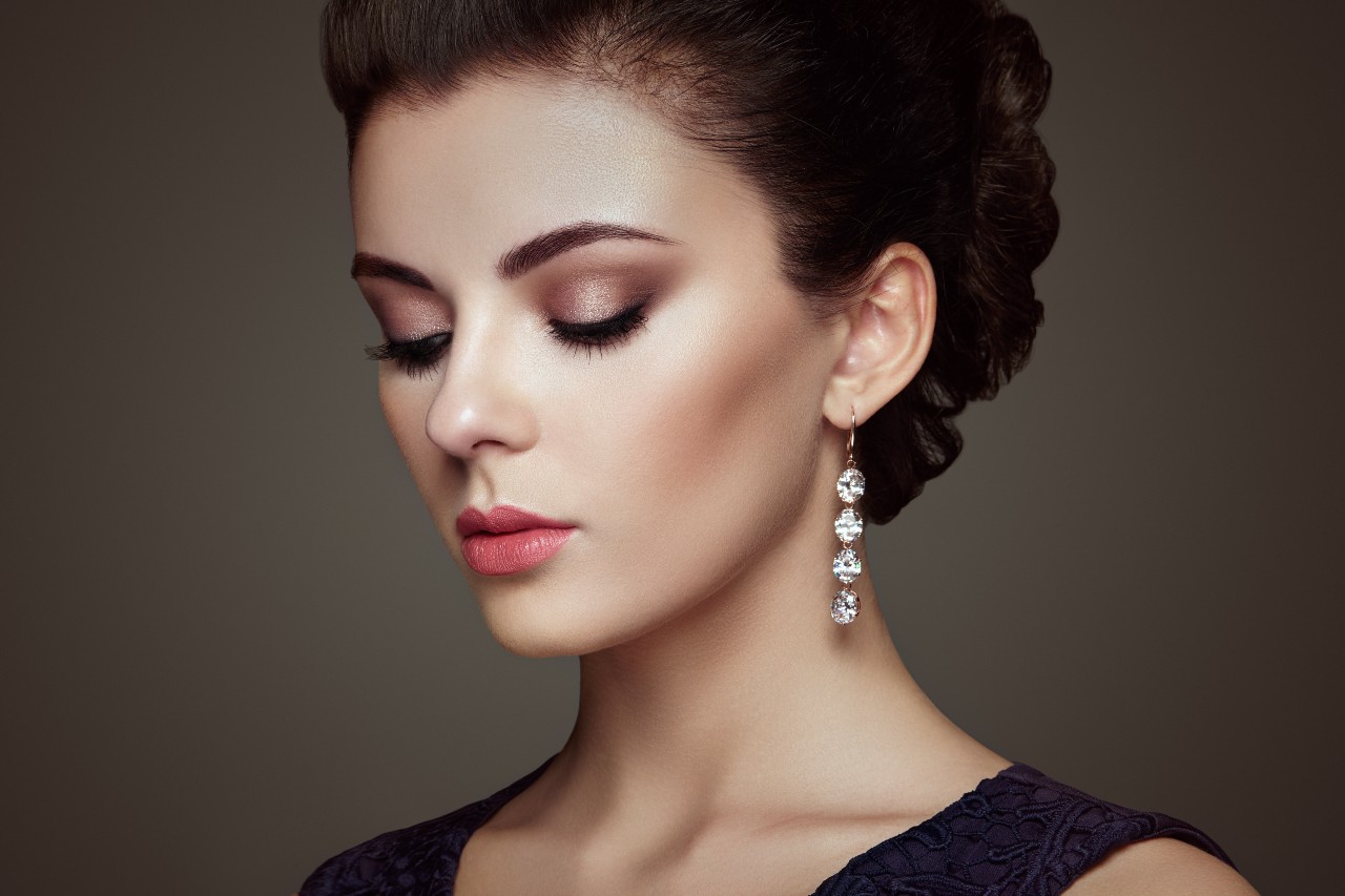 A model looks down while wearing drop diamond earrings and a black dress.