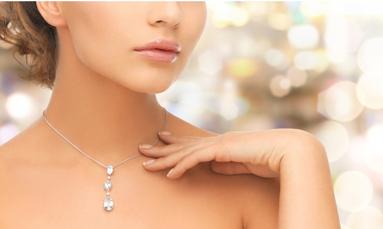 A woman touches her diamond necklace while standing in front of lights.