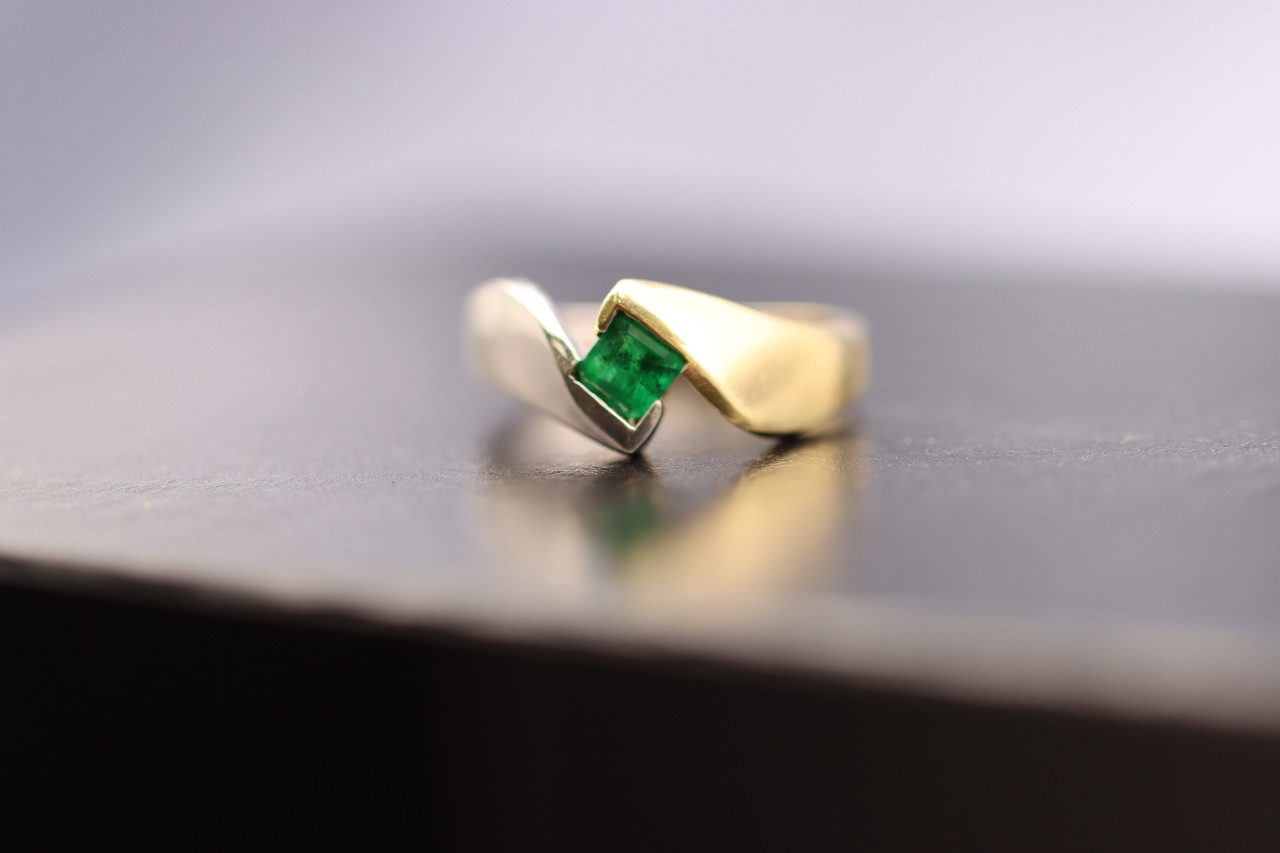 A close-up of a yellow gold fashion ring with a princess cut emerald.