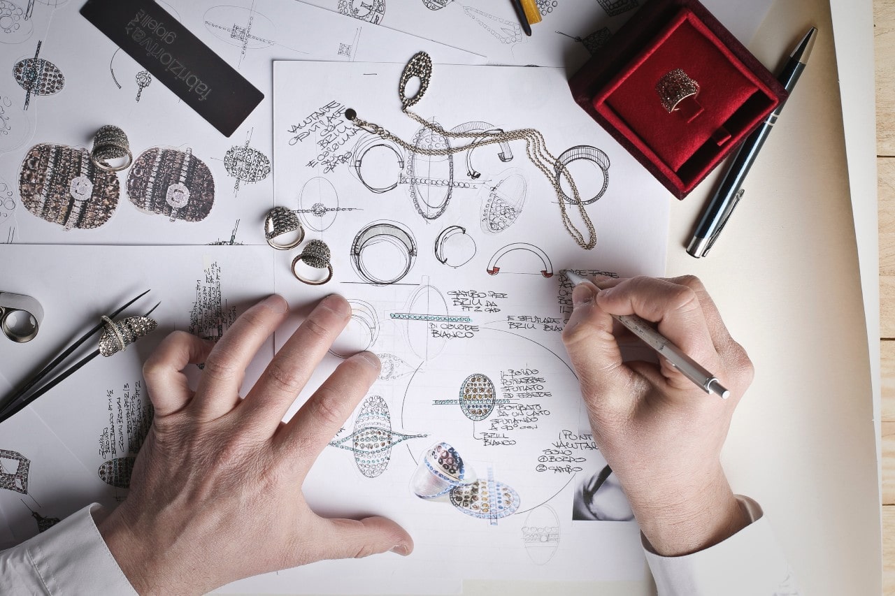 A top-down view of a jeweler sketching out jewelry designs on a large piece of paper.
