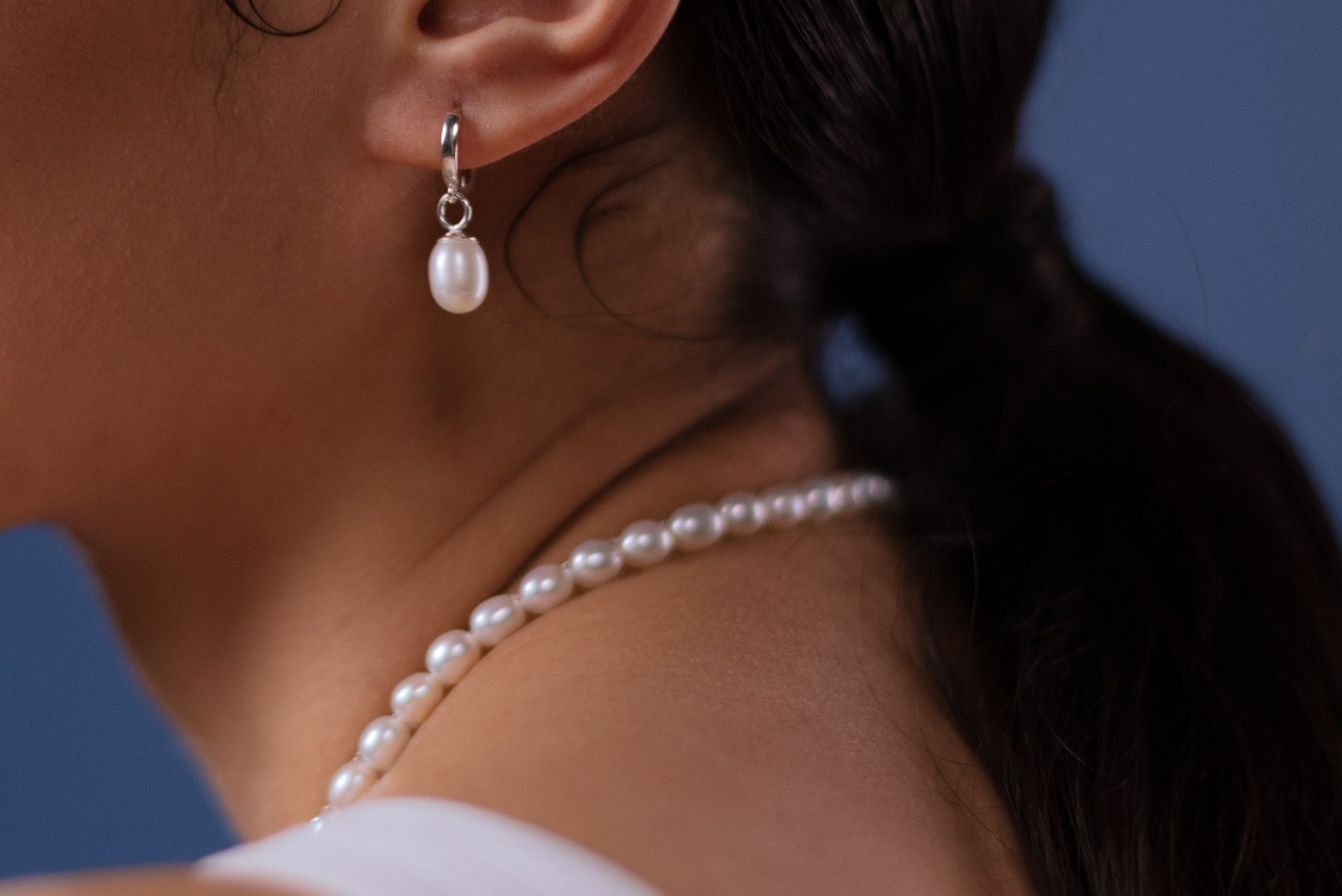 close up image of a woman’s neckline adorned with a pearl necklace and wearing a pearl earring