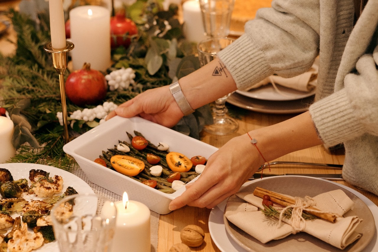 A woman wearing bracelets puts a dish on the Thanksgiving table.