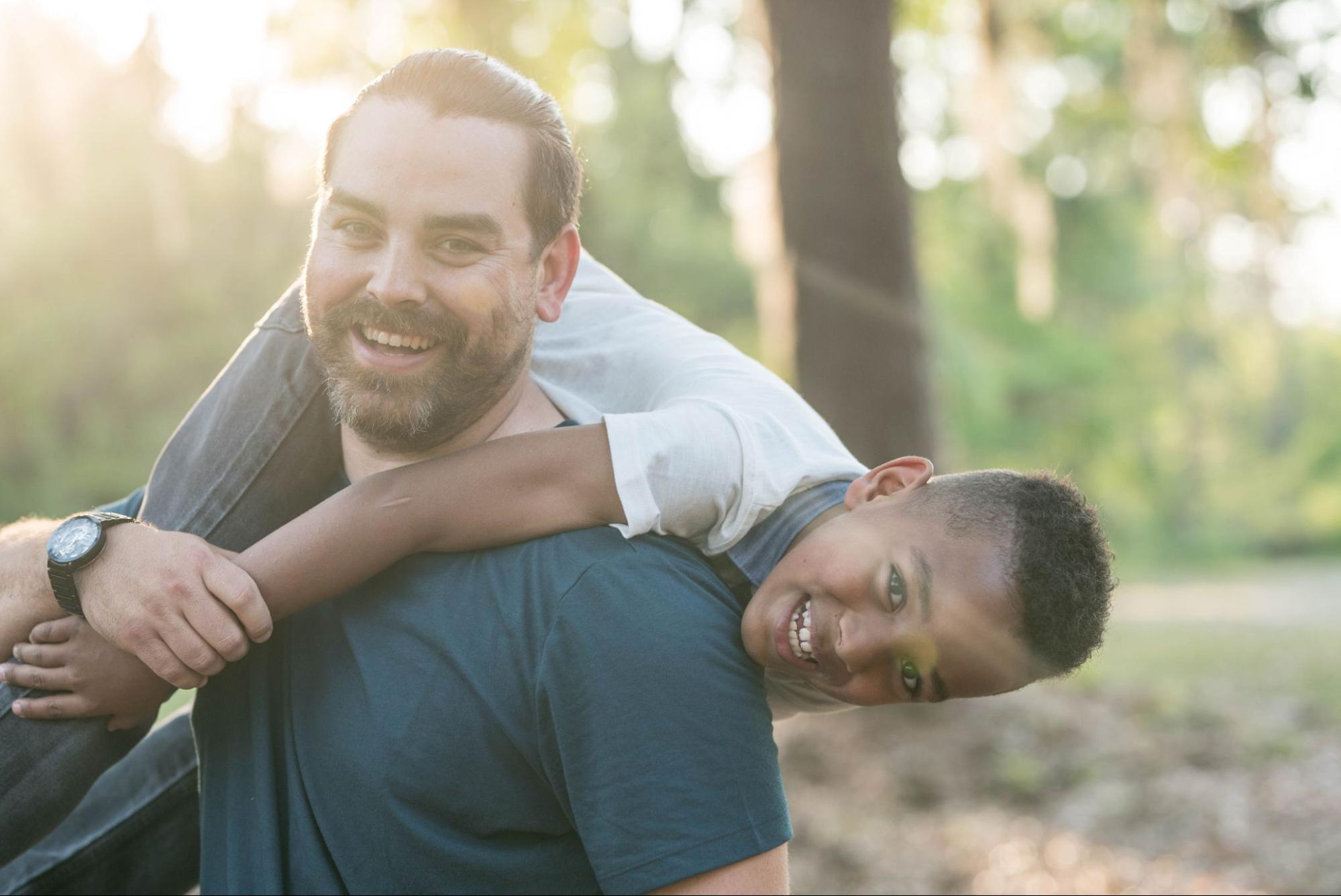 A picture of a happy father wearing a sports watch holding his son over his shoulder.