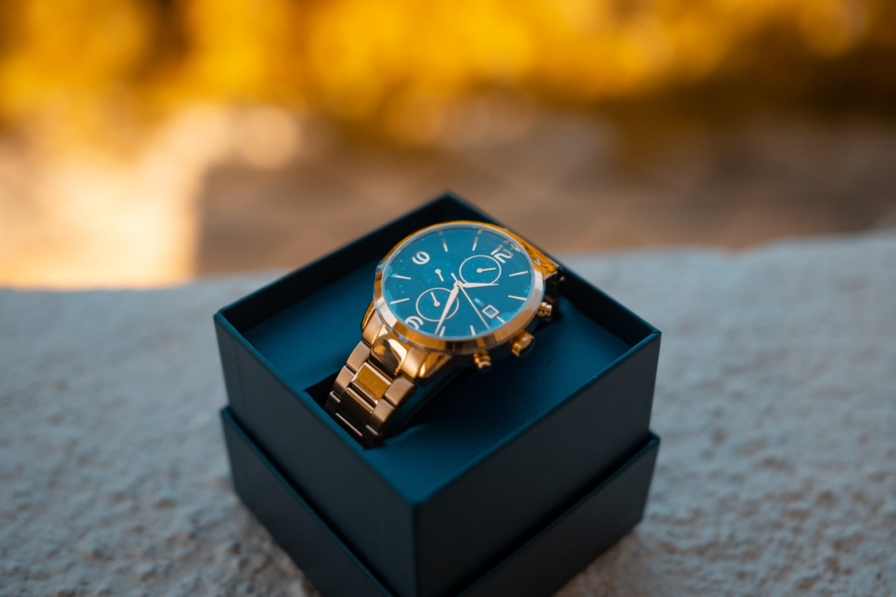 A close-up of a luxury sports watch displayed in-box atop a stucco wall.