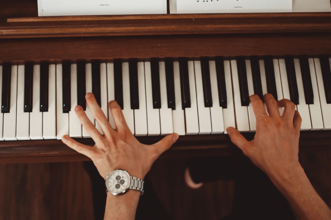 A top-down view of a man wearing a luxury watch as he plays the piano.