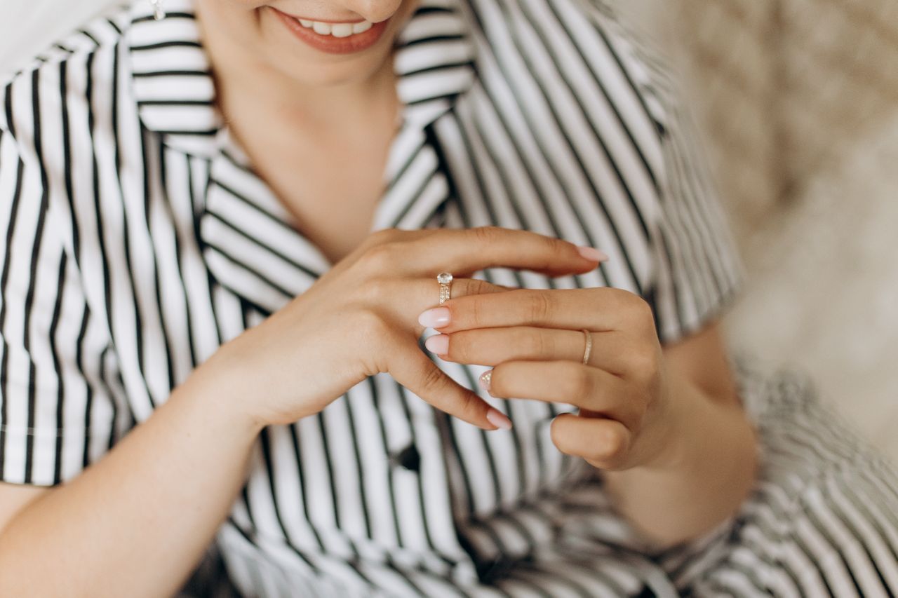 A close-up of a smiling woman wearing a striped shirt admiring a sparkling diamond ring on her finger.