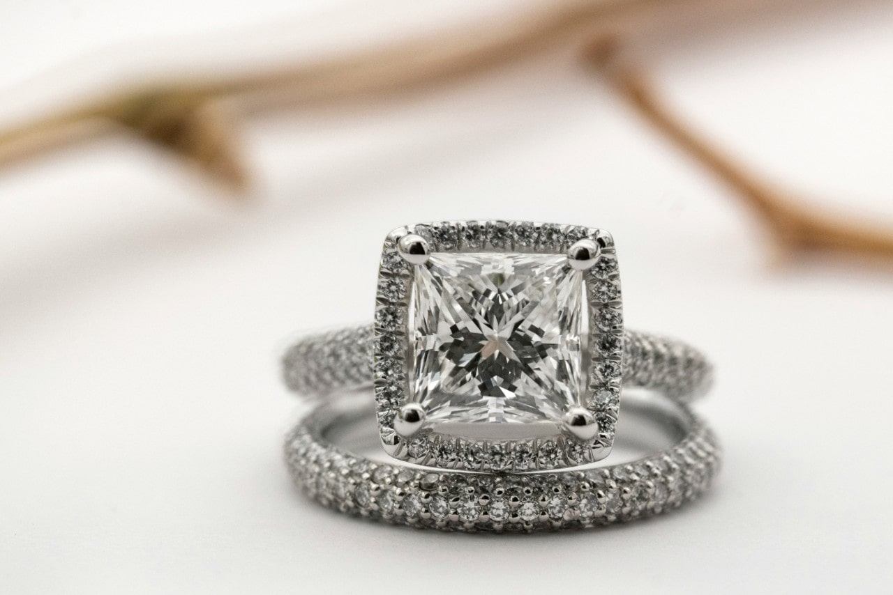 A close-up of a sparkling cushion cut diamond engagement ring accented with smaller diamonds, displayed atop a matching diamond wedding band.