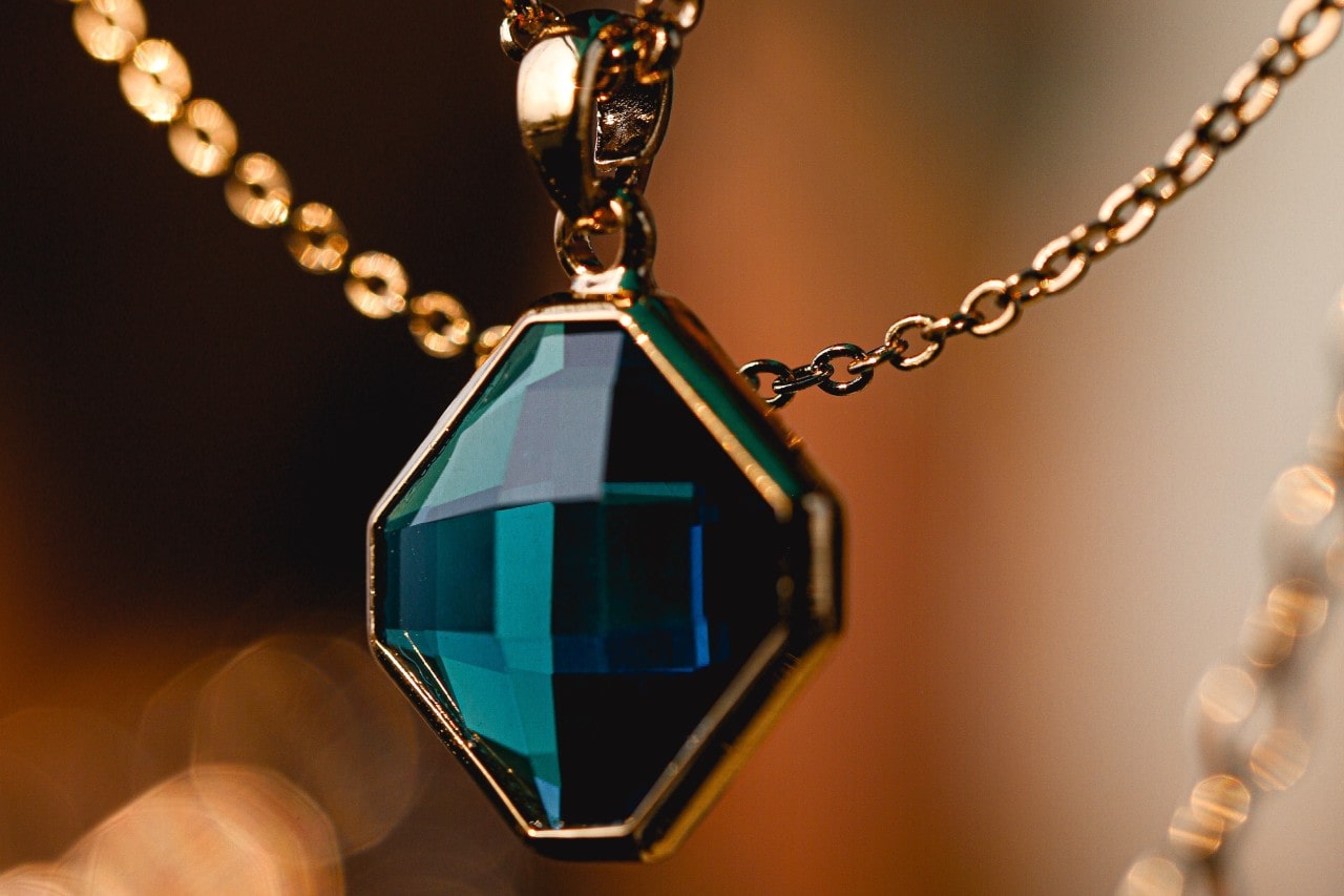 close up image of a yellow gold pendant necklace with a deep teal gemstones