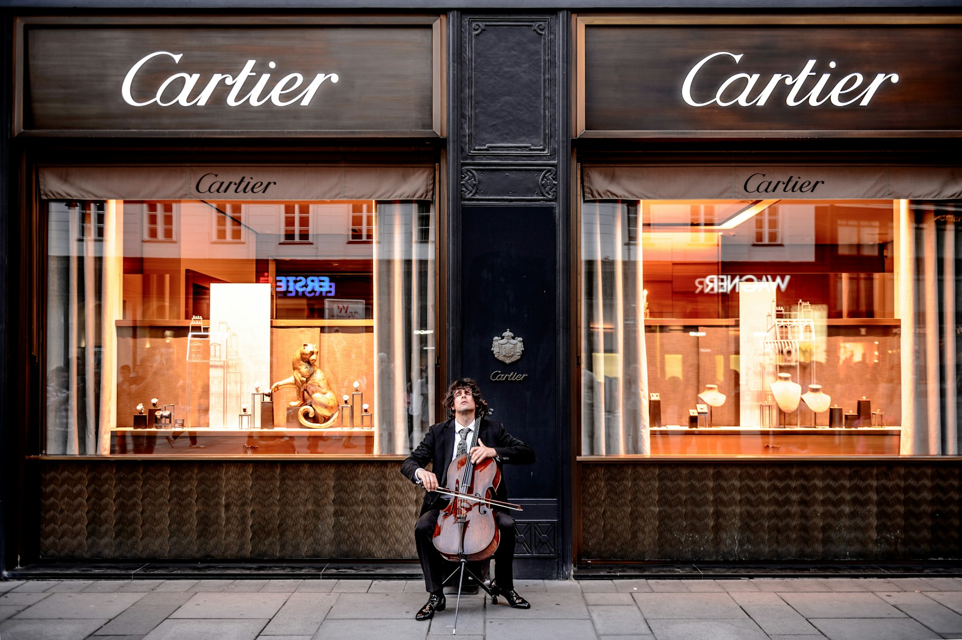 A cellist in formal attire plays outside a luxurious Cartier store with illuminated display windows.