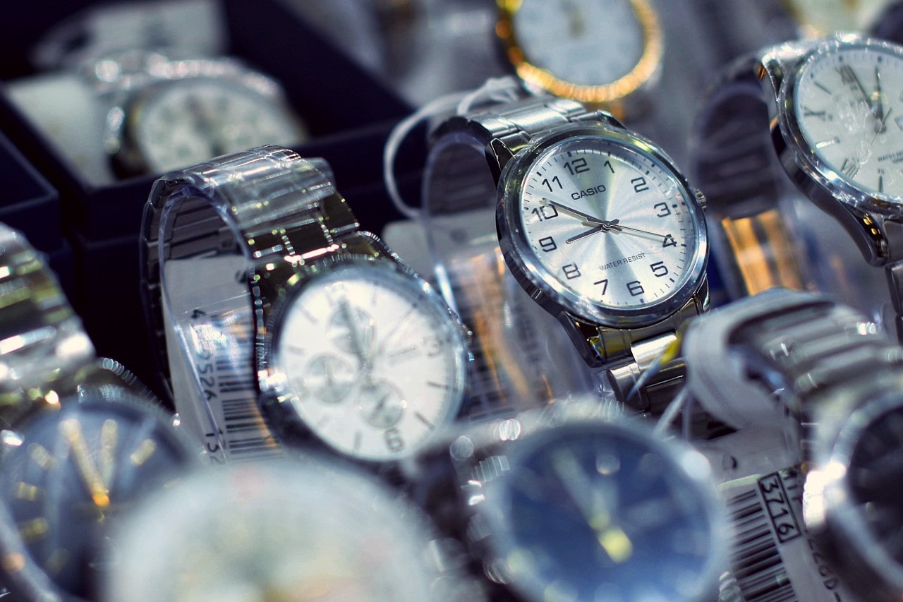 Close-up of various wristwatches displayed in a store. Central focus on a silver watch with a white face and black numerals.