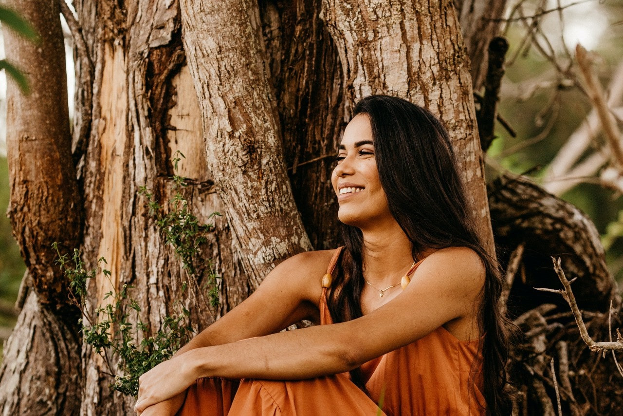 lady sitting against a tree smiling and wearing a Simon G. necklace