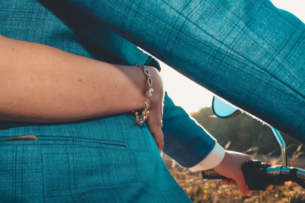 a couple on a scooter, the woman wrapping her arms around the man, wearing a gold bracelet