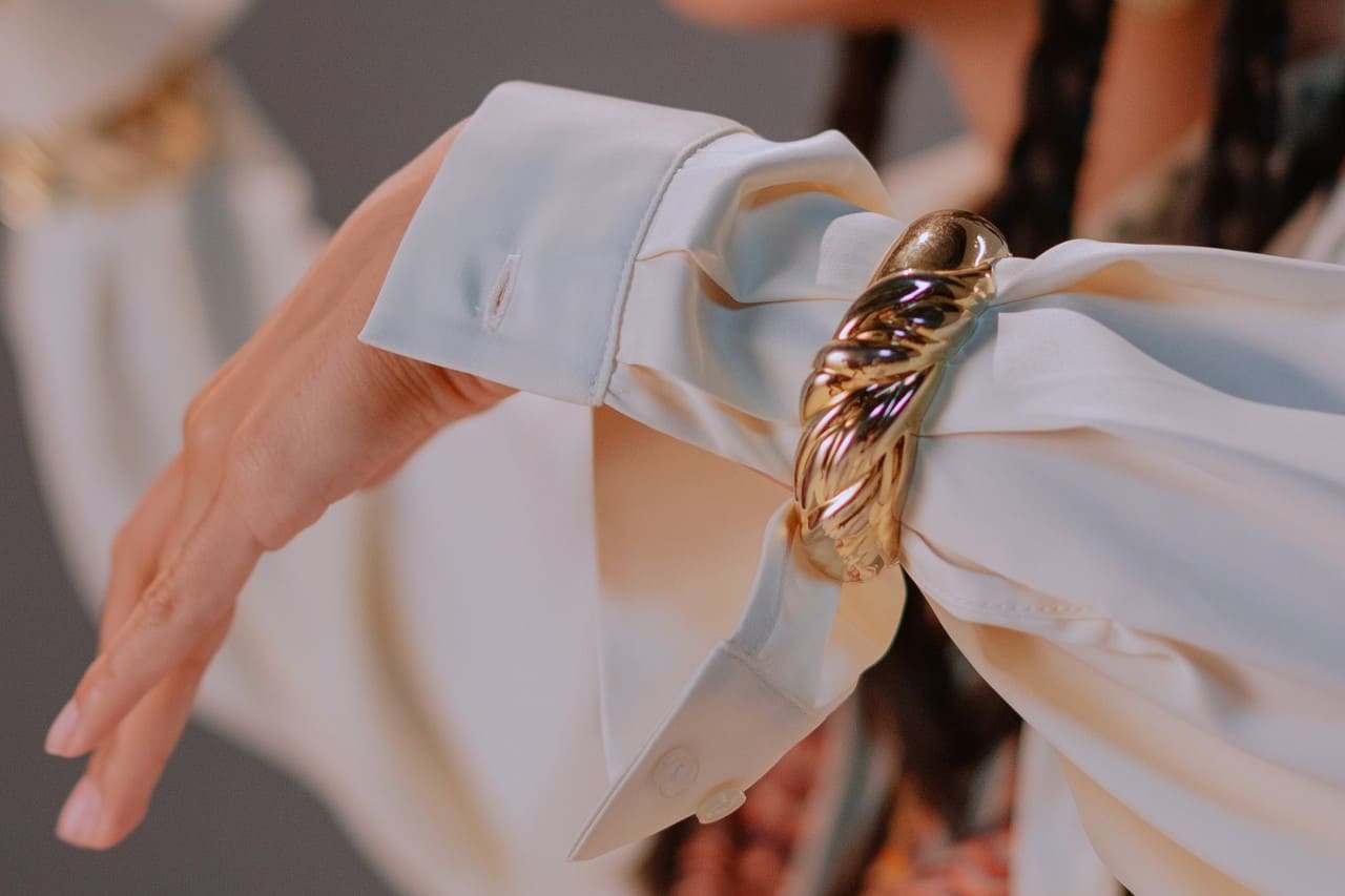a woman’s arm donning a white sleeve and chunky yellow gold bangle bracelet