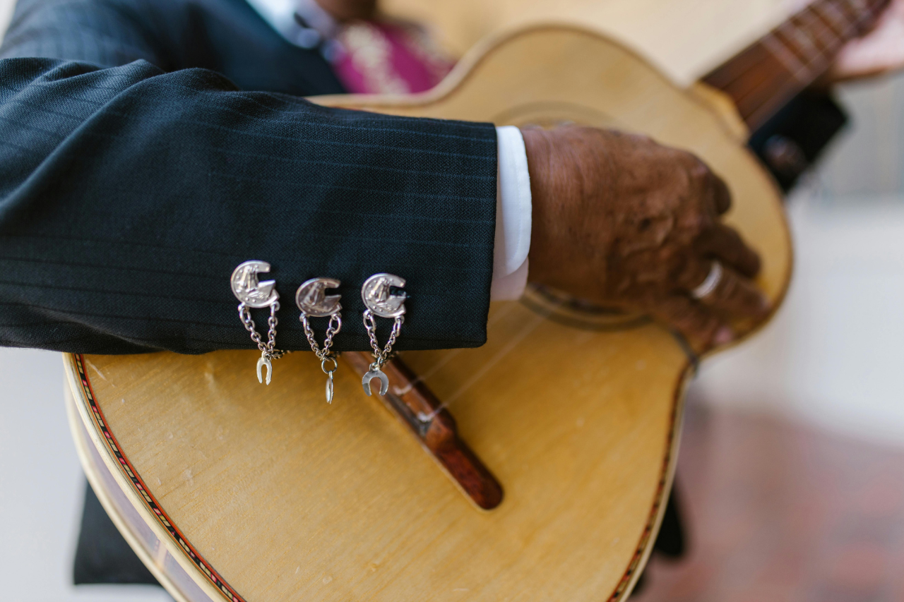 A close-up of a man’s hand as he plays the guitar, his jacket sleeve adorned with three identical, eclectic cufflinks. A close-up of a man’s hand as he plays the guitar, his jacket sleeve adorned with three identical, eclectic cufflinks.