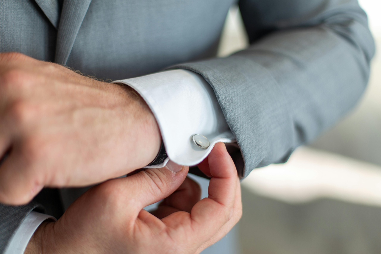 A close-up of a well-dressed man in a grey suit adjusting his sleeve cuffs adorned with sleek and simple cuff links. A close-up of a well-dressed man in a grey suit adjusting his sleeve cuffs adorned with sleek and simple cuff links.