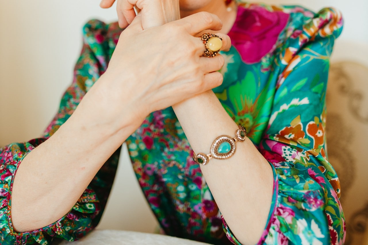 a woman wearing a colorful blouse, turquoise bracelet, and gemstone fashion ring.