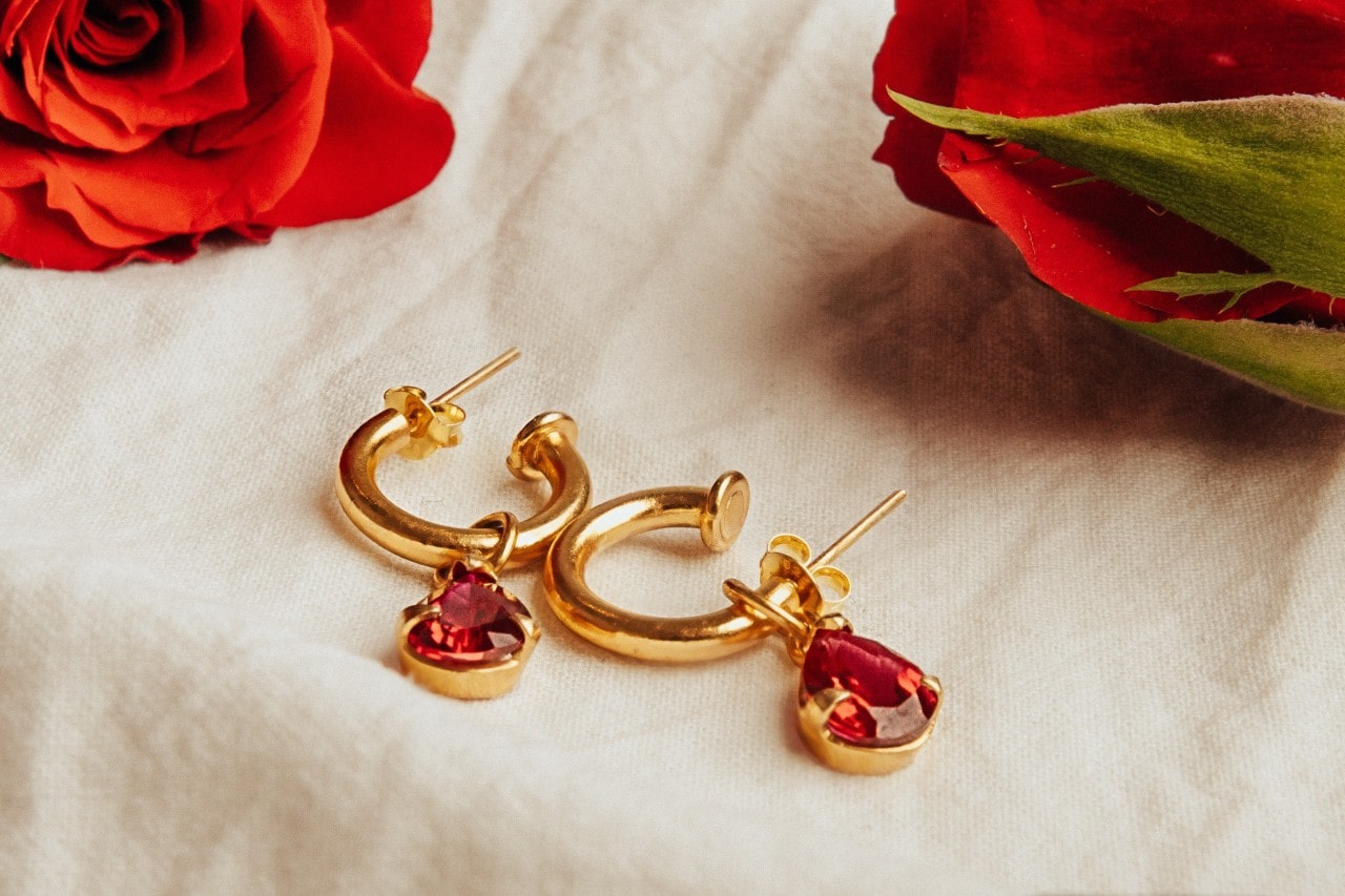 a pair of gold and ruby hoop earrings on a linen cloth.