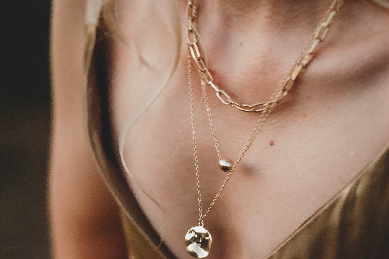 close up image of a woman’s neckline, wearing three gold necklaces.