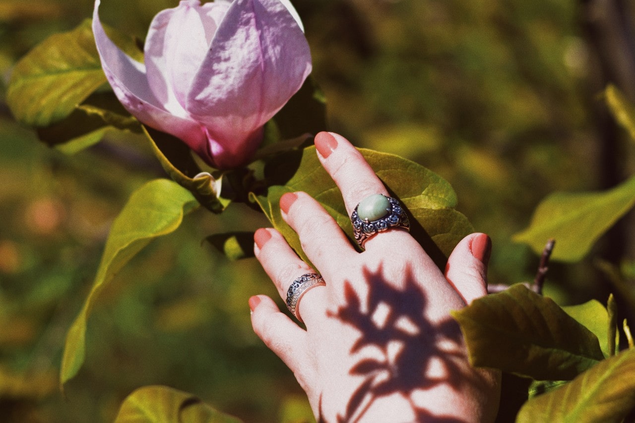 A woman touches a flower wearing three vintage-inspired fashion rings.