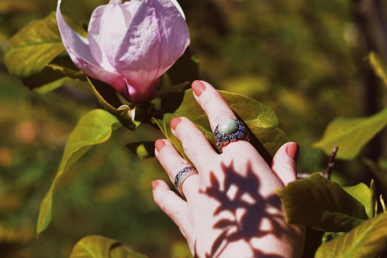 A woman touches a flower wearing three vintage-inspired fashion rings. A woman touches a flower wearing three vintage-inspired fashion rings.
