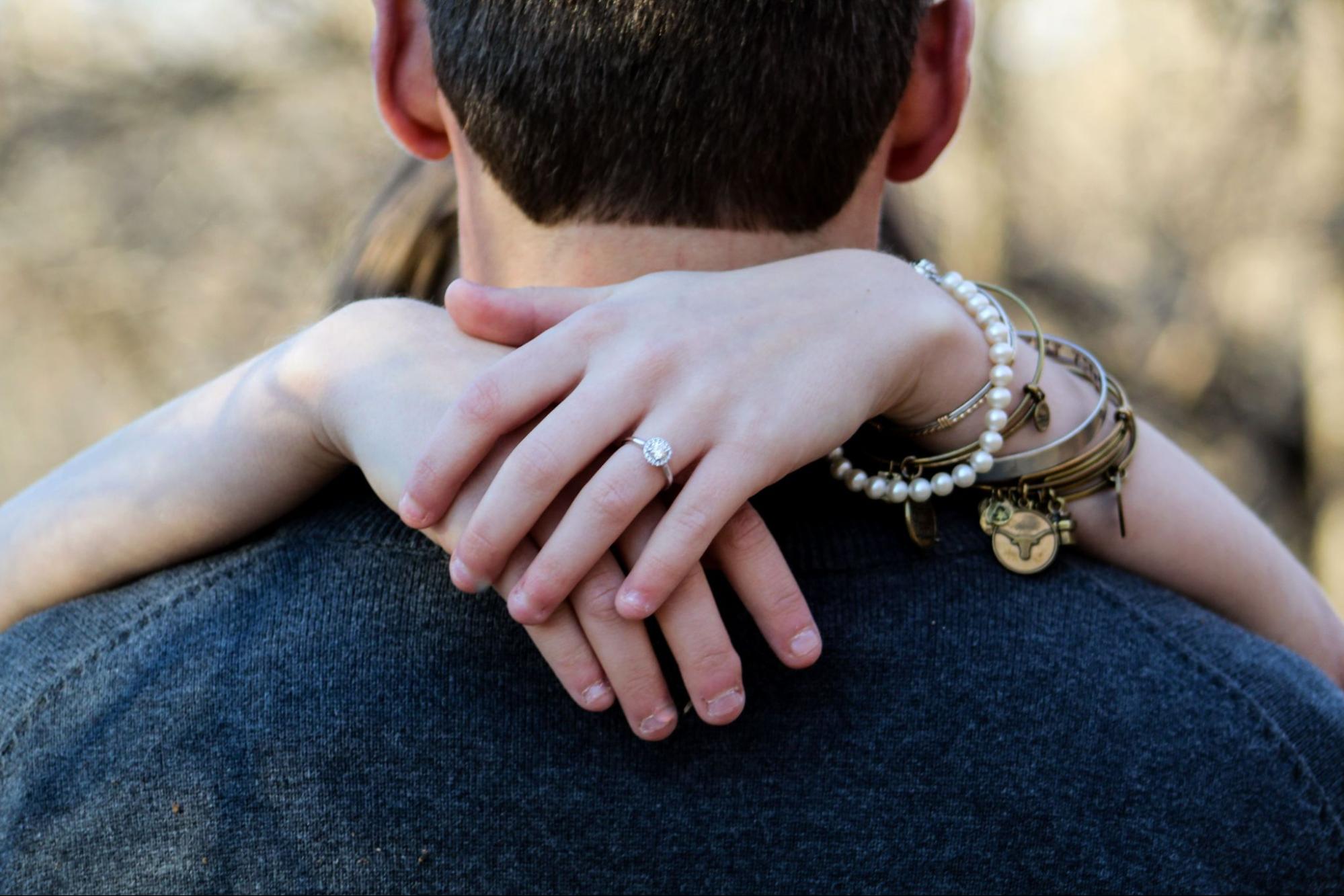 A woman hugs her fiance while wearing multiple bracelets.