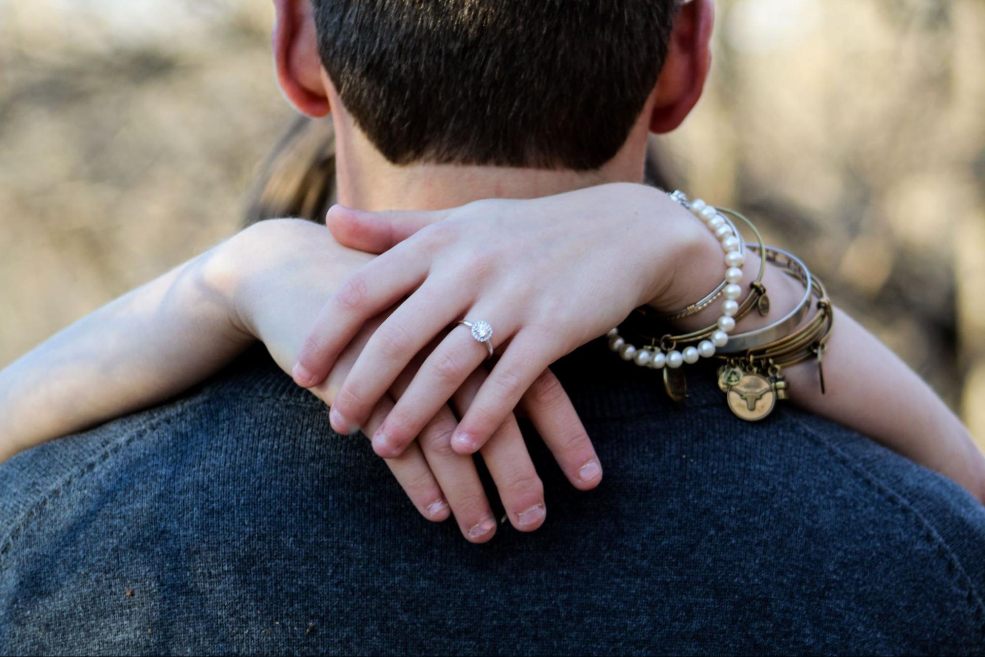 A woman hugs her fiance while wearing multiple bracelets. A woman hugs her fiance while wearing multiple bracelets.