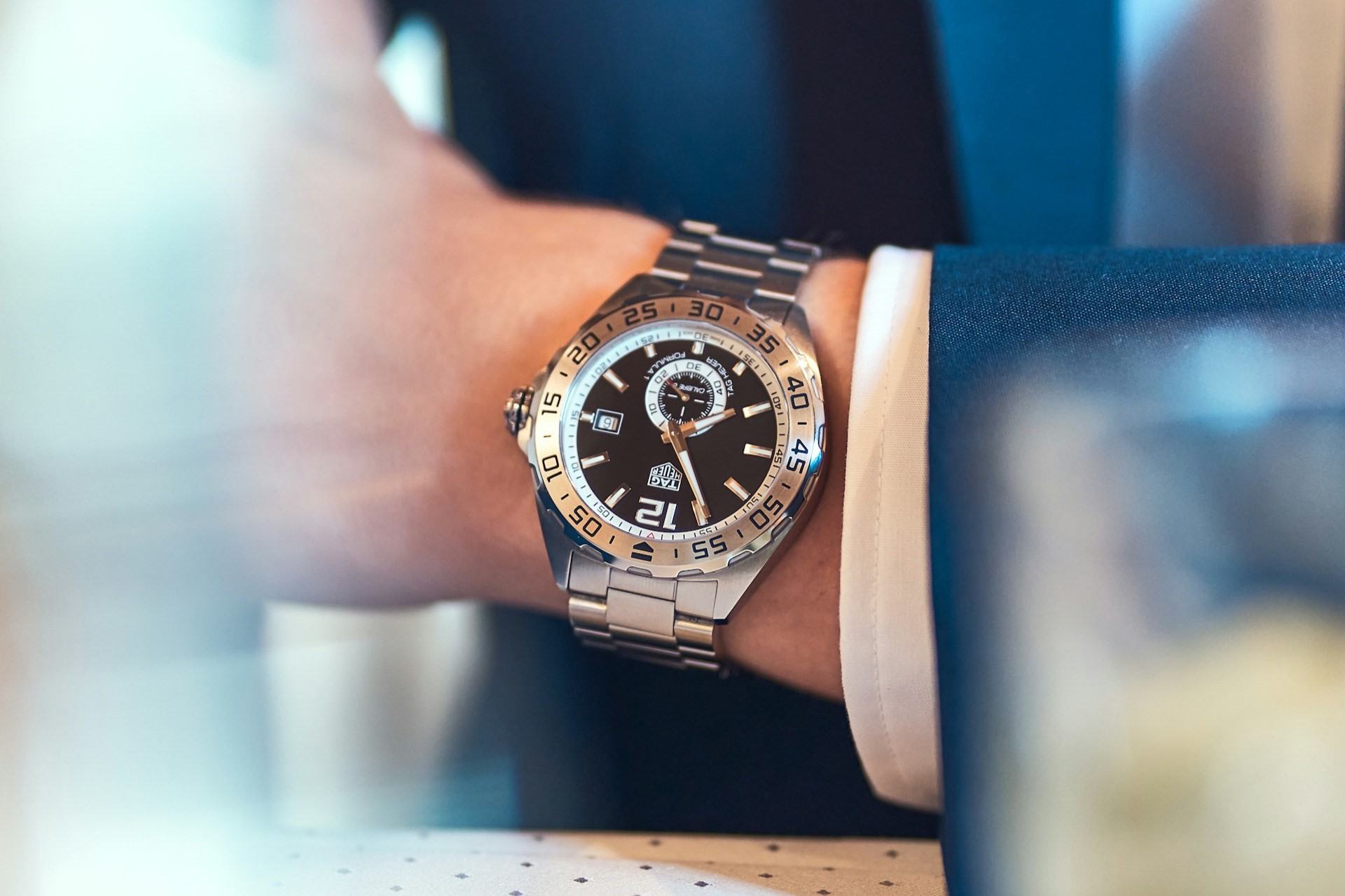 A close-up of a man in a blue suit’s wrist, clad in a TAG Heuer luxury watch. A close-up of a man in a blue suit’s wrist, clad in a TAG Heuer luxury watch.