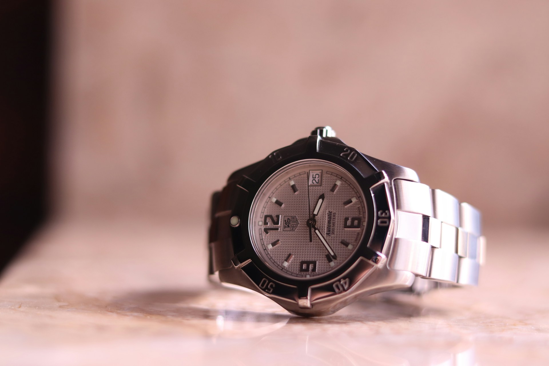 A close-up of a TAG Heuer watch displayed on its side on a marble surface. A close-up of a TAG Heuer watch displayed on its side on a marble surface.