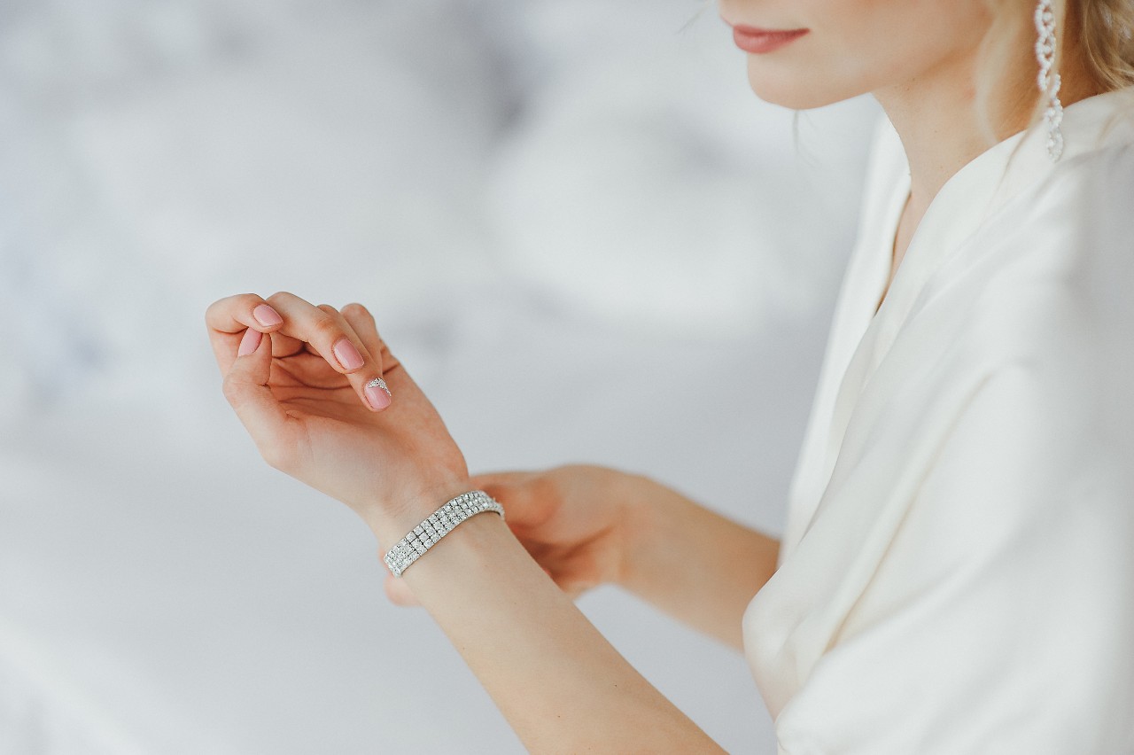 A close up of a woman in a white silk robe fixing her diamond tennis bracelet