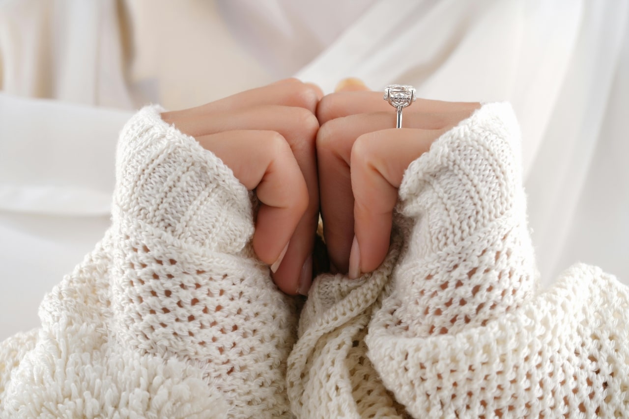A close-up of a woman wearing a chunky knit sweater, with emphasis on her elegant engagement ring. A close-up of a woman wearing a chunky knit sweater, with emphasis on her elegant engagement ring.