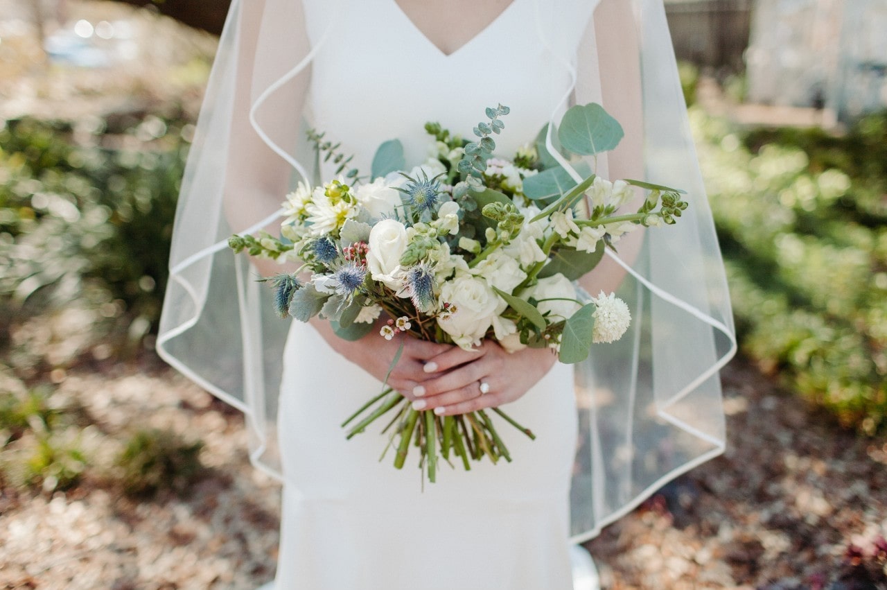 A close-up of a bride holding a delicate bouquet, her engagement ring visible on her hand. A close-up of a bride holding a delicate bouquet, her engagement ring visible on her hand.