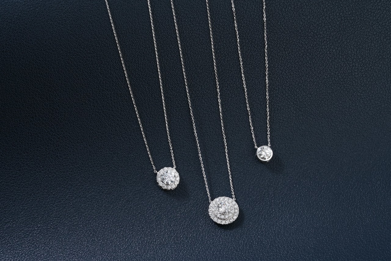 Three different sized diamond pendants laid neatly on a dark leather surface. Three different sized diamond pendants laid neatly on a dark leather surface.