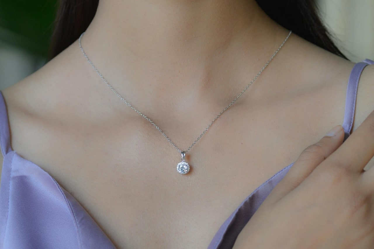 A close-up of a woman’s neck wearing a diamond pendant and a lavender dress. A close-up of a woman’s neck wearing a diamond pendant and a lavender dress.