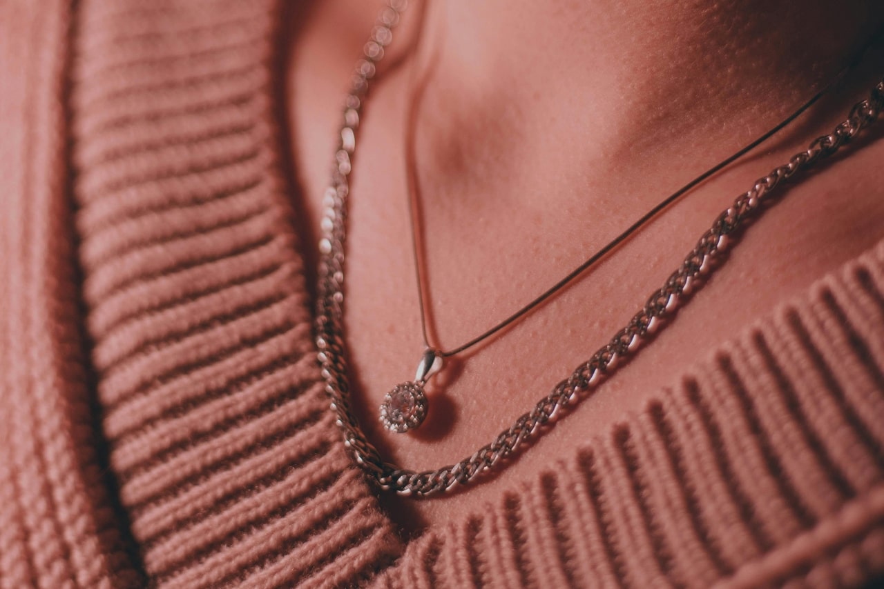 A close-up of a woman wearing a diamond pendant and a chain stacked, the image has a red hue. A close-up of a woman wearing a diamond pendant and a chain stacked, the image has a red hue.