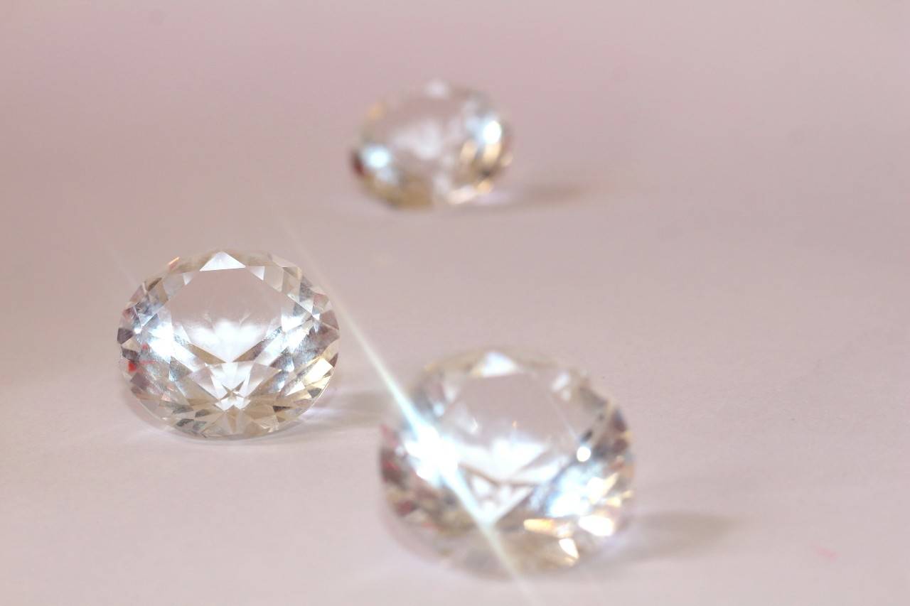 A close-up of three glistening round cut diamonds on a dusty pink backdrop.