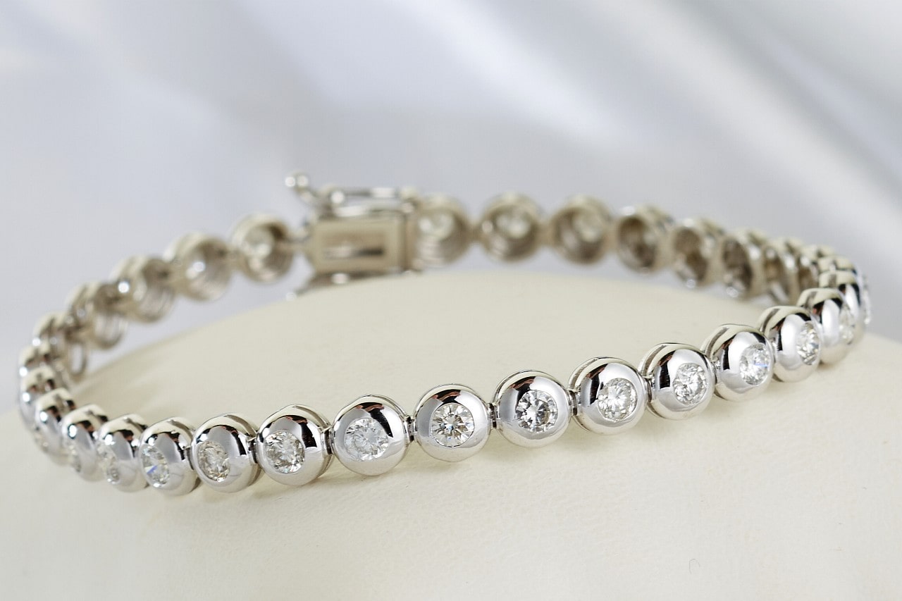A close-up image of a white gold diamond bracelet with bezel set gems. A close-up image of a white gold diamond bracelet with bezel set gems.