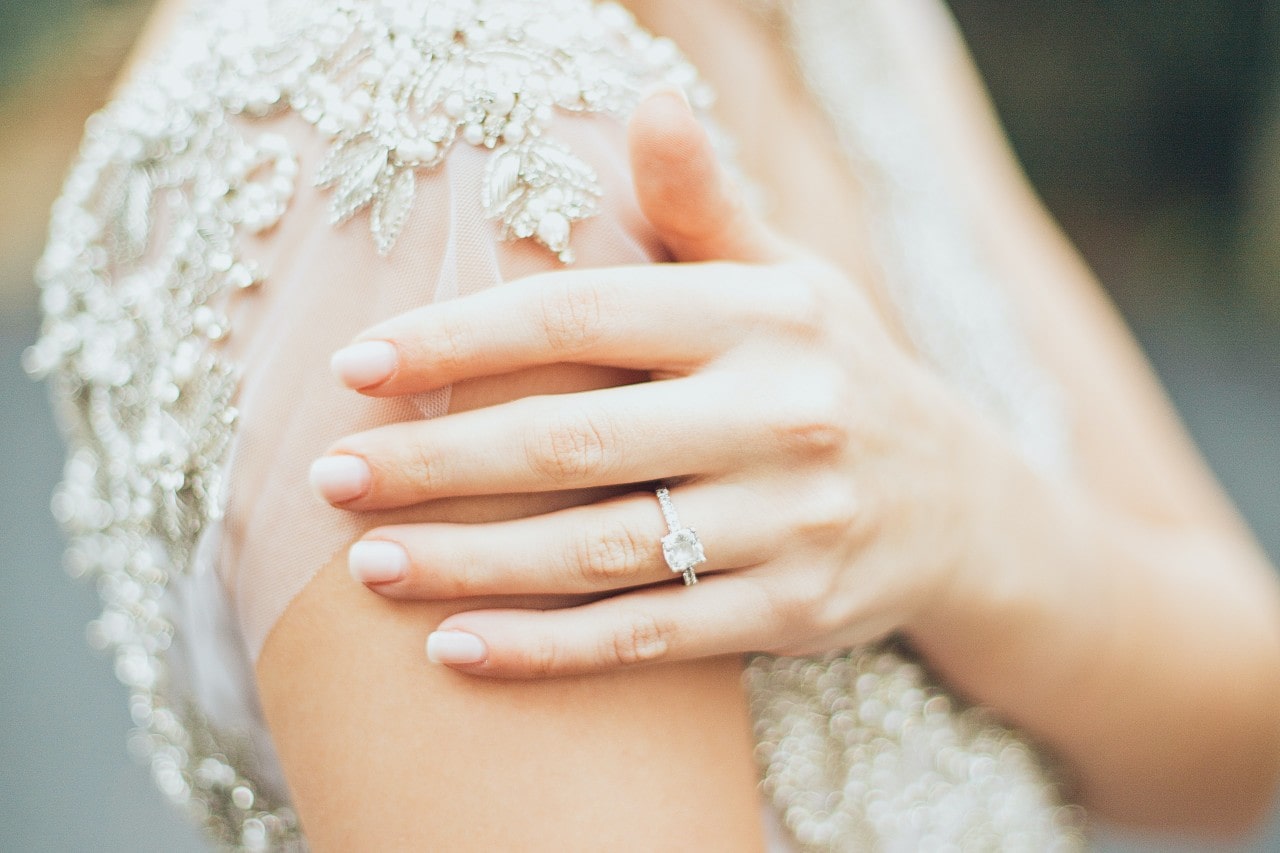 A bride rests her hand on her shoulder, showing off her side stone ring.