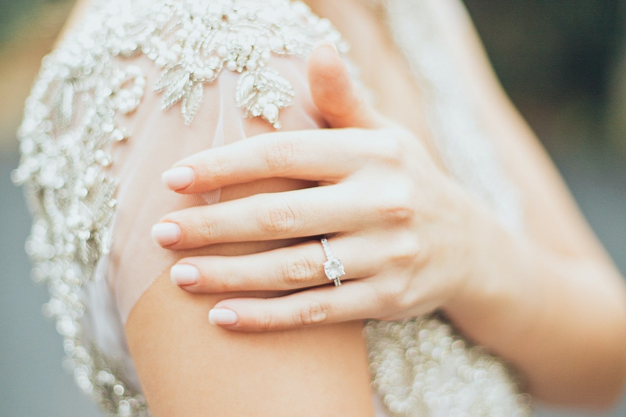 A bride rests her hand on her shoulder, showing off her side stone ring. A bride rests her hand on her shoulder, showing off her side stone ring.