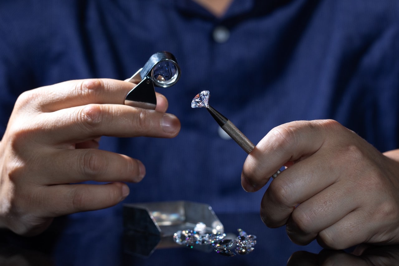 A close up of jeweler’s hands inspecting loose diamond through a magnifying lens.