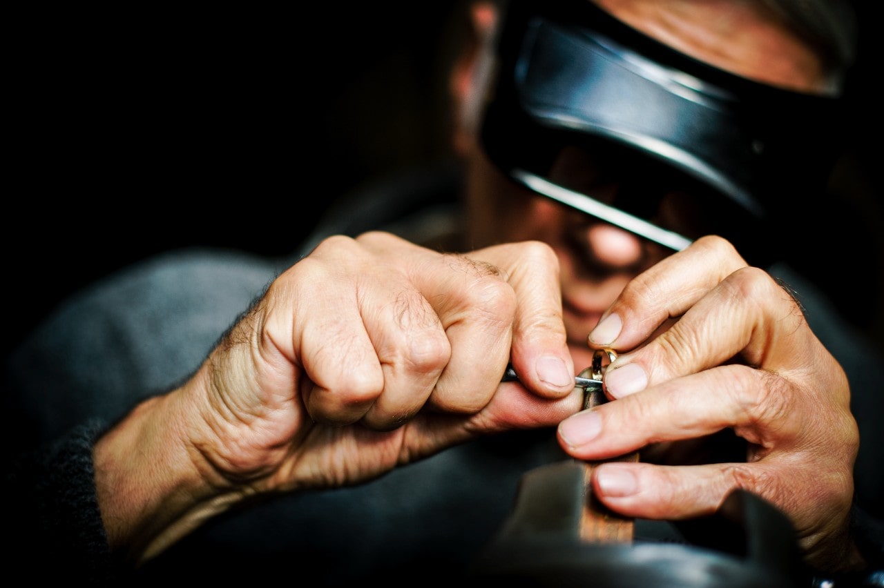 A jeweler carefully repairing a yellow gold wedding band.