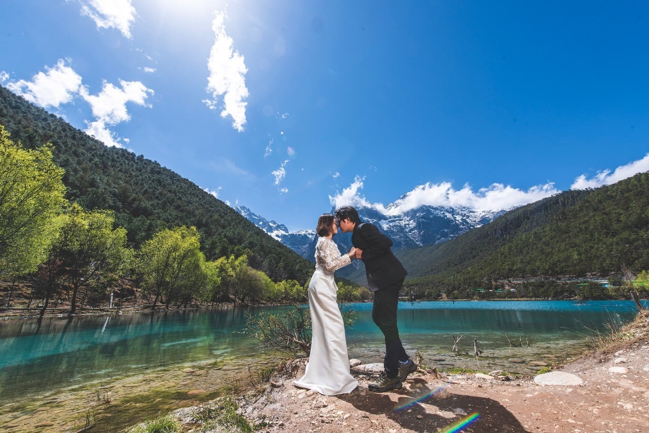 a bride and groom embracing by a beautiful mountain and lake